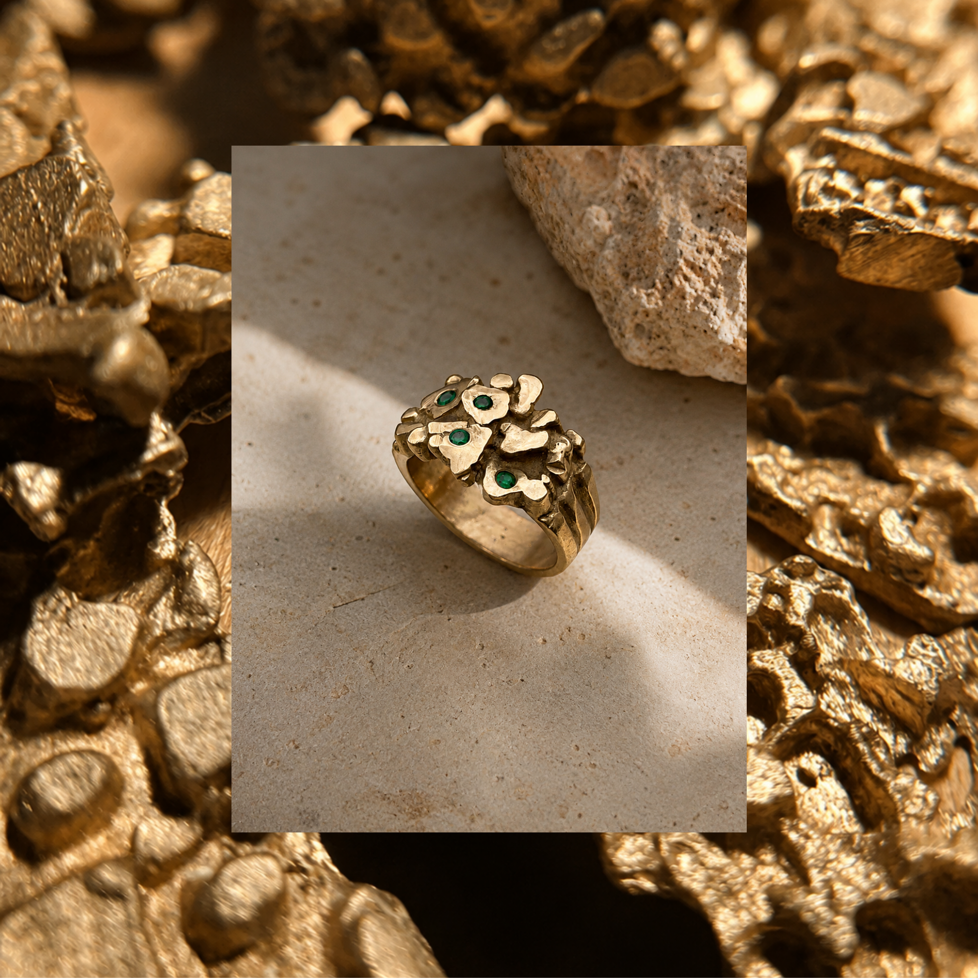 A gold and silver abstract ring with green gemstone accents, presented on a black square card against a textured gold background.